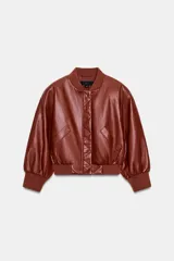 Chaqueta corta estilo bomber de Zara, confeccionada en material efecto piel color marrón rojizo. Presenta cuello redondo, hombreras, mangas abullonadas con puños elásticos y cierre frontal con cremallera oculta y botones a presión. Incluye bolsillos delanteros de vivo.