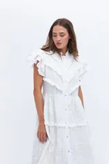 Vestido midi de lino blanco con diseño de broderie, cuello alto, cierre frontal con botones y volados decorativos en los hombros y el cuerpo.