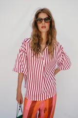 Camisa de corte oversize con estampado de rayas verticales rojas y blancas. Presenta cuello solapa, escote en pico y mangas largas abullonadas con puños elásticos.