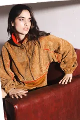 Buzo marrón de pana con cierre frontal parcial, cuello alto, bolsillo tipo canguro con solapa y cordón ajustable en el ruedo.