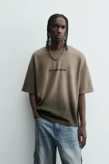 Camiseta de corte relajado (relaxed fit) con cuello redondo y manga corta. Presenta un estampado frontal con relieve en la zona del pecho con el texto "Endless Echo", y un efecto de teñido degradado que va del marrón claro al marrón oscuro/negro en la parte inferior.