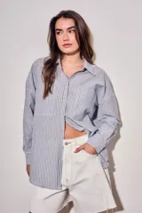 Camisa de corte oversize con diseño de rayas verticales en tonos azul y blanco. Presenta cuello clásico, cierre frontal con botones y mangas largas con puños abotonados.