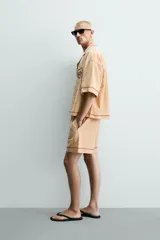 Shorts relaxed fit color beige con textura en relieve tipo jacquard, cintura elástica con cordón ajustable y detalle de bordado en contraste en el bajo.