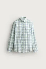 Camisa de corte regular fit con cuello abotonado, manga larga y bolsillo de parche en el pecho. Presenta un diseño a cuadros en tonos verdes y azules sobre fondo blanco, con un sutil efecto arrugado en el tejido.
