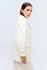 Tapado color crema con cuello solapa, cierre con botones y bolsillos laterales. Presenta detalle de costuras en contraste en cuello, puños y solapa.