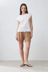 Blusa blanca de algodón con frente de tela broderie, cuello redondo y mangas cortas con diseño de hombros caídos.