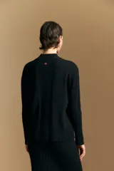 Polera de cuello alto confeccionada en tejido de punto negro, con diseño de textura acanalada en cuello, puños y ruedo, y trama vertical en mangas y espalda.