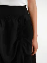 Pollera midi de diseño desestructurado en color negro, con cintura elastizada y detalles fruncidos con cordones ajustables a los lados.