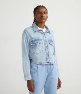 Camisa cropped de jeans celeste con cuello solapa, abotonada al frente, con bolsillos delanteros, desgastes y barra redondeada.