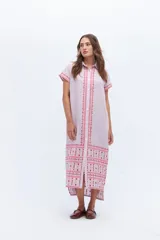 Vestido camisero de lino color lila con bordados rojos en contraste. Presenta un diseño de largo midi con cuello camisero, cierre frontal de botones y mangas cortas. Los detalles bordados recorren la botonadura, los puños y el ruedo de la prenda.