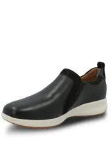 Zapatilla tipo slip-on Hush Puppies de cuero negro con cierre lateral decorativo, diseño de perfil clásico y suela de goma blanca con base antideslizante.