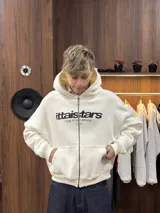 Buzo con cierre frontal completo, capucha amplia y bolsillos tipo canguro. Presenta estampado gráfico en el pecho con la marca IttaiStars y diseño de corte holgado.