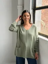 Sweater de punto color verde, con escote en V, mangas largas con puños acanalados y dos bolsillos frontales. Presenta una costura vertical central decorativa.
