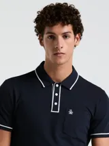 Polo de piqué azul marino de manga corta con cuello y borde de mangas con línea blanca. Tiene tapeta con tres botones blancos y bolsillo en el pecho con logo de pingüino bordado en blanco.