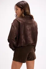 Campera de gamuza color beige con diseño de calados florales en hombros y espalda, cierre frontal y cuello camisero. Presenta un corte relajado y textura suave.