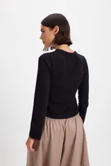 Blusa de algodón con cuello redondo, manga larga y cierre frontal con botones a tono. Presenta un diseño ajustado al cuerpo.