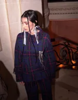 Sweater oversize de lana natural con estampado cuadrillé en tonos azul, verde y rojo. Presenta cuello alto, mangas largas y detalles de flecos torneados en el cuello, puños y dobladillo.