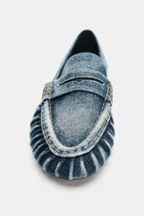 Mocasín plano confeccionado en efecto denim, con diseño de antifaz en el empeine, detalles fruncidos en la parte delantera y punta redonda.