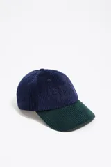 Gorra de béisbol confeccionada en pana, con diseño bicolor que combina una corona azul marino y una visera verde oscuro. Presenta un bordado tonal en el frente y ojales de ventilación.