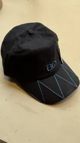 Gorra negra con bordado de las iniciales BG en el frente y diseño de costuras geométricas en la visera.