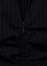Vestido corto de estilo camisero, color negro con estampado de rayas verticales finas. Presenta cierre frontal con cremallera, detalle de fruncido central, cuello camisero y mangas largas con puños abotonados.