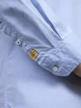 Camisa celeste de manga larga con cuello abotonado y bolsillo en el pecho.