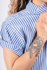 Conjunto de camisa y shorts a rayas verticales celestes y blancas. La camisa es de manga corta y se usa abierta sobre un top blanco.