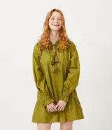 Vestido corto de manga larga en color verde oliva, confeccionado en tejido plano con hilos metalizados a contraste. Presenta cuello redondo con lazo decorativo y flecos, mangas largas con puños elásticos y detalle de volados en los puños.