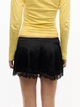 Minifalda de satén color negro, de tiro bajo y calce evasé, con cintura elastizada, cierre lateral invisible y detalle de encaje en el ruedo.