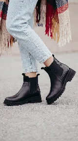 Bota tipo Chelsea de cuero negro con paneles elásticos laterales y suela track dentada. Presenta un diseño minimalista con tirador en la parte trasera.