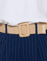 Pantalón wide leg blanco con finas rayas verticales oscuras, tiro alto, bolsillos laterales y pinzas frontales. Incluye un cinturón trenzado de rafia con hebilla rectangular.
