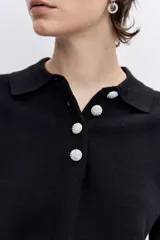 Sweater de punto negro con cuello polo y cierre frontal de botones, de manga larga y calce holgado.