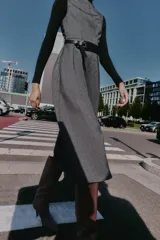 Vestido midi jaspeado en tonos grises, con cuello redondo, manga sisa y bajo en evasé. Incluye un cinturón ancho negro con hebilla rectangular y cierre de cremallera oculta en la espalda.