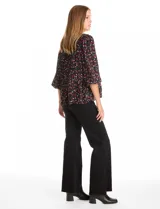 Blusa de gasa con estampado de corazones rojos y blancos sobre fondo negro. Presenta cuello redondo con escote en V, mangas largas con puños fruncidos y un corte holgado con detalle de frunces en la cintura.