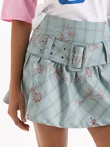 Minifalda celeste con estampado a cuadros y detalles ilustrados, de corte corto, con un cinturón ancho incorporado de la misma tela con doble hebilla forrada.