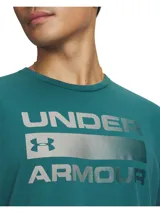 Remera de manga corta Under Armour color verde petróleo, con estampado frontal del logo y nombre de la marca en tono metalizado sobre una franja horizontal. Confeccionada en tejido Charged Cotton de secado rápido y elástico.