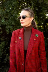 Blazer de corte sastrero con estampado cuadrillé en tonos rojos y negros, con solapas clásicas y cierre frontal. Presenta detalles de pines decorativos en las solapas.