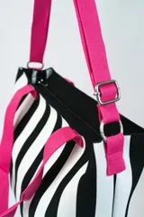 Bolso tipo tote bag con diseño a rayas verticales blancas y negras, doble asa de mano rosa y correa de hombro ajustable y removible también rosa.