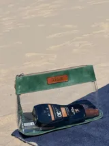 Neceser transparente con detalles en cuero verde y cierre superior con cremallera.