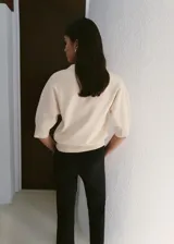 Cardigan de punto fino color crudo, con cuello en V, mangas cortas y cierre frontal con un botón joya en forma de flor.
