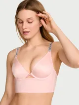 Bralette longline de microfibra color rosado, con aros, copas sin forro, escote en V y tirantes ajustables con logo de pedrería. Presenta un detalle de aberturas entrecruzadas en el centro delantero y silueta alargada.
