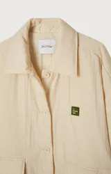 Chaqueta capitoneada color crema, de corte oversize, con cuello camisero, cierre frontal con botones a presión, bolsillos de parche y puños con abertura.