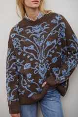 Buzo de tejido de punto en color marrón con un patrón ornamental floral en color celeste. Presenta cuello redondo, mangas largas y un corte holgado.