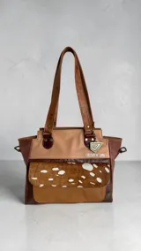 Cartera tipo tote de cuero en combinación de tonos marrones y beige, con diseño estructurado, doble asa de hombro, bolsillo frontal con solapa de pelo con estampado animal print, herrajes metálicos y llavero decorativo de la marca.