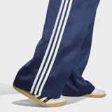 Pantalón deportivo Adidas SST de satén color azul marino, de corte holgado y diseño de pernera ancha. Cuenta con las clásicas tres tiras blancas a lo largo de los laterales y el logo del trifolio bordado en una pierna.