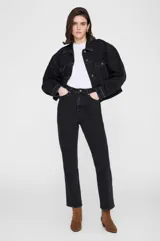 Chaqueta de denim negra de corte relajado, con cuello clásico, cierre frontal con botones metálicos y bolsillos con solapa en el pecho.
