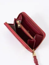 Billetera compacta de cuero vacuno color bordó, con cierre perimetral, correa de muñeca y aplique metálico dorado en forma de mariquita en el frente.