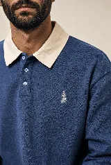 Buzo de manga larga estilo rugby color azul petróleo, con cuello beige en contraste, tapeta con botones y pequeño bordado en el pecho. Confeccionado en algodón pesado con fit relajado.