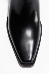 Botas Chelsea negras de cuero con punta cincelada y elásticos laterales. Tienen un taco cuadrado y trabillas de tela en la parte delantera y trasera del cuello.