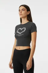 Remera de algodón gris oscuro con efecto gastado, corte crop y mangas cortas. Presenta un estampado frontal que simula un corazón formado por eslabones de cadena y texto debajo.